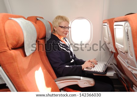 smiling businesswoman posing with laptop on the board of plane in ecomomy class of aeroflot