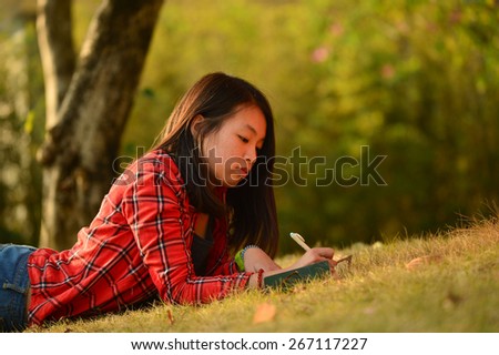Pretty young chinese woman lie on the grass in the park and make notes in the notebook