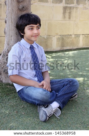 young brown haired boy sitting cross-legged by a tree