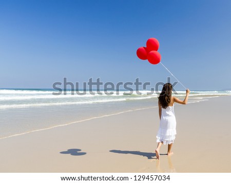 Beautiful girl walking in the beach and holding red balloons