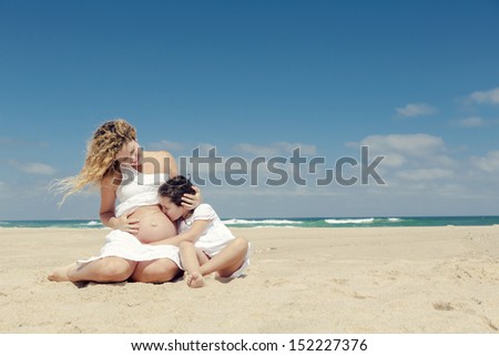 Beautiful pregnant woman and her little daughter kissing mom\'s belly