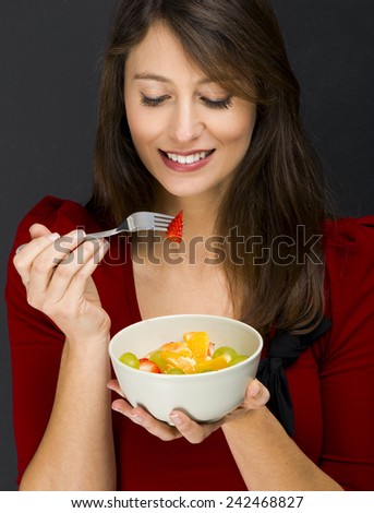 Beautiful young woman eating a fruit salad, over a black background