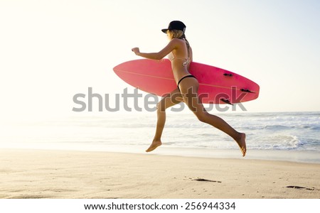 Hot surfer girl jumping on the beach at the sunset and holding a surfboard