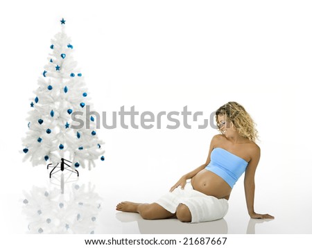 Beautiful pregnant woman seated on the floor near a white christmas tree