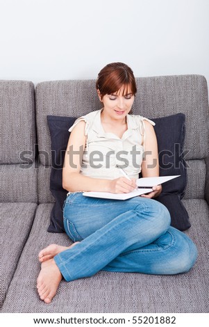 Woman sitting on couch and writing something on a notebook