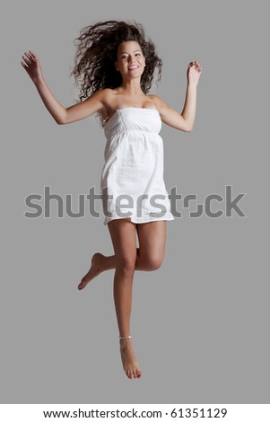 Beautiful and happy young woman jumping over a grey background