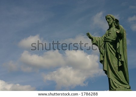 A statue of jesus blessing, against a blue sky with some small white clouds