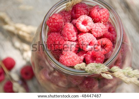 Glass jar of raspberries over old aged wood table with flowers and berries