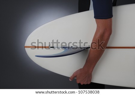 Closeup of a teenage male wearing a wet suit holding a surf board. Horizontal format over a light to dark gray background