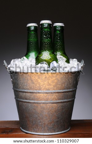 Ice bucket with three bottles of beer on a wet wood bar counter top. Vertical format on a light to dark gray background.