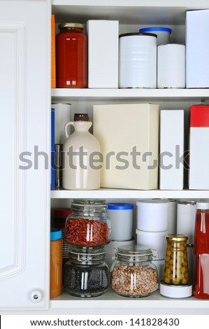 Closeup of a well stocked pantry. One door of the cabinet is open revealing canned goods, condiments, package foodstuffs, and storage jars.