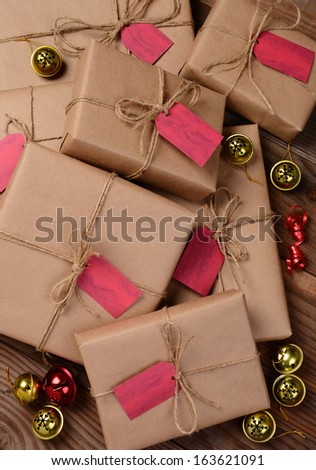 High angle view of a group of holiday gifts wrapped with eco friendly craft paper. Presents have red gift tags and are surrounded by jingle bells and ribbon. Vertical Format.