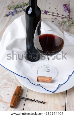 High angle wine and flower still life. Glass of red wine and bottle on a towel and wood rustic table. Vertical format.