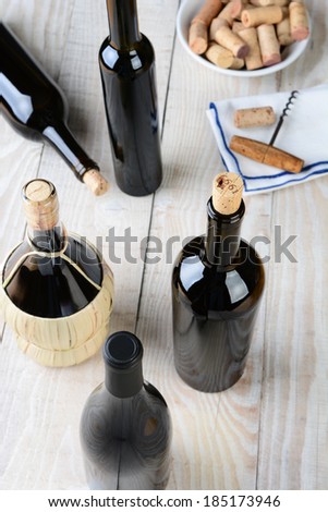 Wine still life shot from a high angle. Five bottles of wine with a cork screw napkin and bowl of corks on a rustic farmhouse style table. Vertical format.