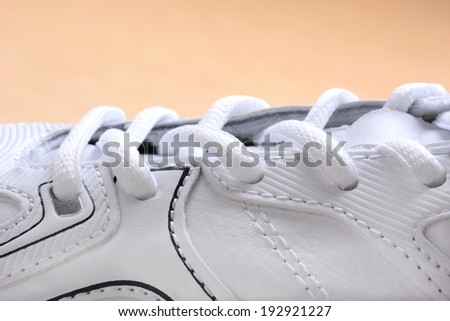 Closeup of laces on a brand new sneaker. The athletic shoe is all white as are the laces, horizontal format on a wood floor.
