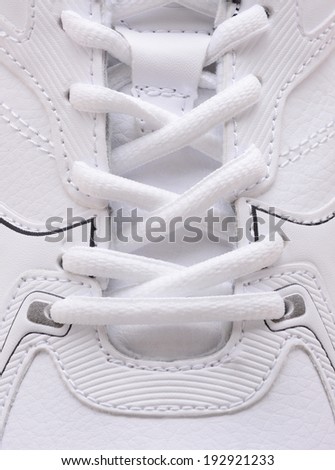 Closeup of the laces on a brand new sneaker. The athletic shoe is all white as are the laces filling the vertical frame.