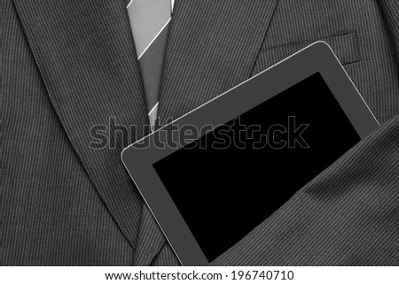 Closeup of a business jacket with white shirt and tie with one arm over a tablet computer. the empty suit is laid out and ready for the day. The screen is blank., Horizontal format.