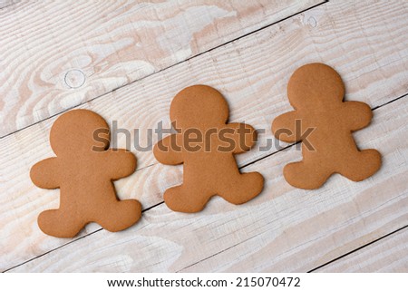 HIgh angle view of three gingerbread men on a rustic white kitchen table. The cookies are  plain and without icing.