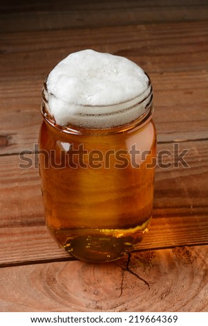 Glass of beer in a country bar setting served in a canning jar. Vertical format on a rustic wood background.