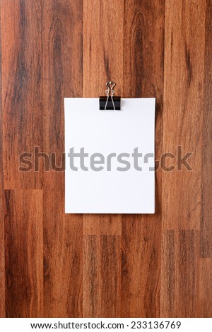 Blank sheets of paper held by a clip hanging from a nail in the middle of a dark wood wall. Vertical format. The blank white paper is ready for your copy.