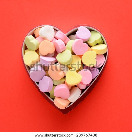 High angle view of a bunch of pastel candy hearts in a heart shaped box for Valentines Day. Square format on a red background, the candies are blank.