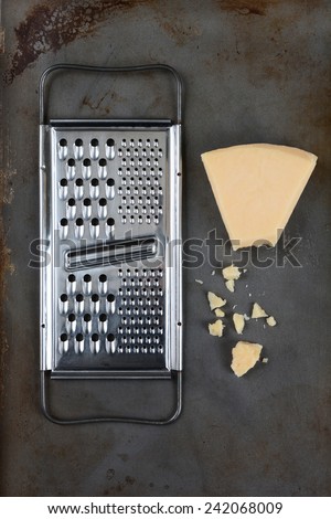 High angle shot of a broken wedge of Parmesan cheese and grater on used baking sheet. Vertical format.