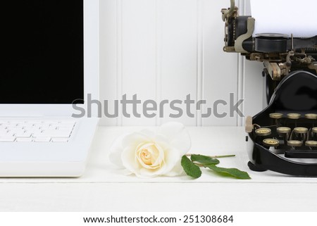 Closeup of a white desk with a rose laying between a modern laptop computer and an antique typewriter. Only half of the laptop and typewriter are shown. Horizontal format.