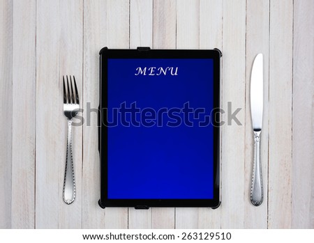 Tablet computer with menu on the screen on a rustic wood restaurant table. Electronic food service ordering concept.
