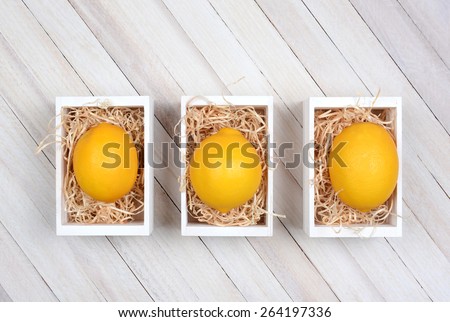 High angle shot of three wooden boxes each with a single lemon on a bed of straw. The wooden crates are on a rustic wood table.