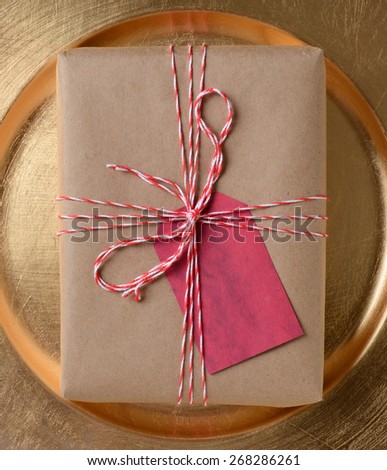Package on a gold platter, The gift is wrapped in plain brown paper and tied with red and white twine. A blank red gift tag is attached to the present.