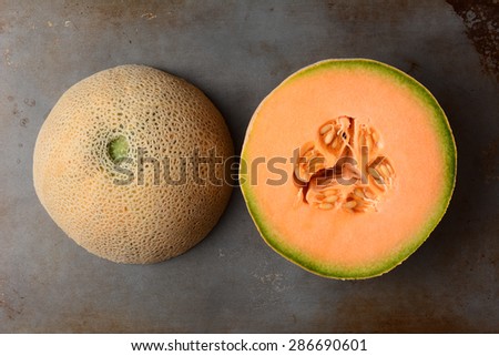 Two halves of the same cantaloupe, the cut side is showing the pulp and seeds, the other half is rind side up. Overhead view in horizontal format.