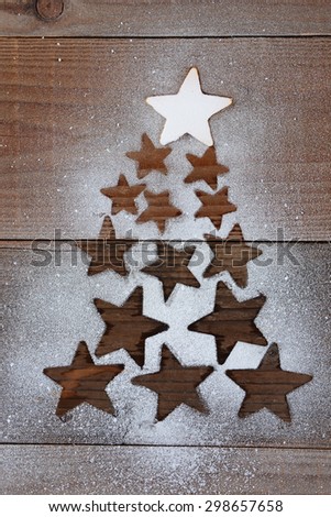 Stars forming a Christmas tree shape on a dark wood table. The top star is covered with snow while the other star shapes are void of snow. Vertical overhead view.