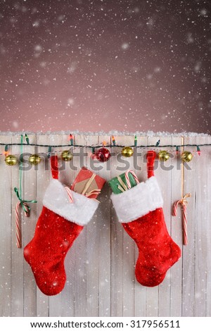 Christmas Stocking hanging on a rustic white fence with lights, jingle bells, and candy canes. Vertical format with snow effect.