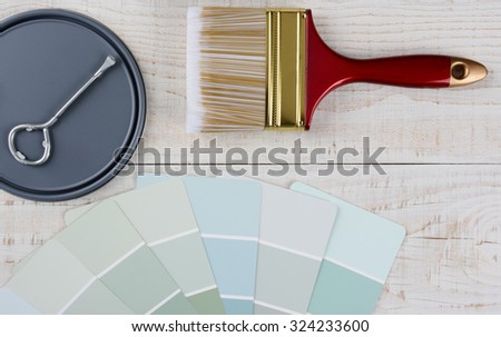 Painting still life with brush, paint chips, paint can lid with opener on a rustic wood surface. Horizontal format.