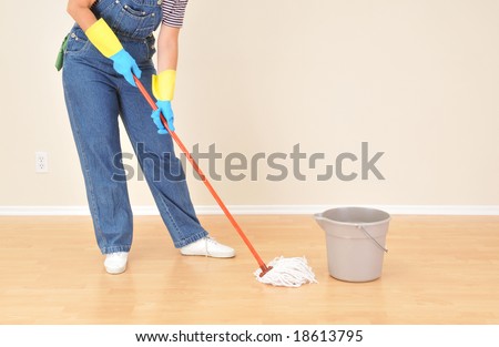 Woman in overalls mopping floor in vacant room.