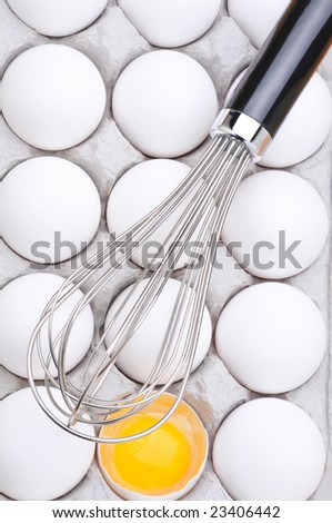 Whisk laying on top of eggs in carton with one broken eggs showing the yolk. Vertical format filling the frame.
