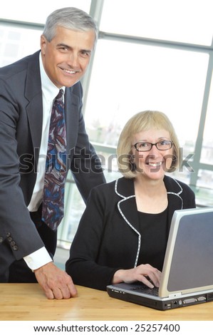 Two Smiling Middle Aged  Business People with Laptop Computer in office setting