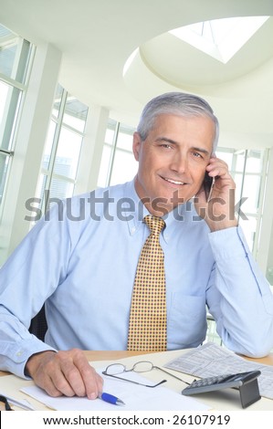 Middle Aged Businessman Sitting at Desk Talking on Cell Phone in office setting