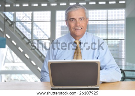 Smiling Middle Aged Businessman at desk in Modern Office Building with Laptop Computer