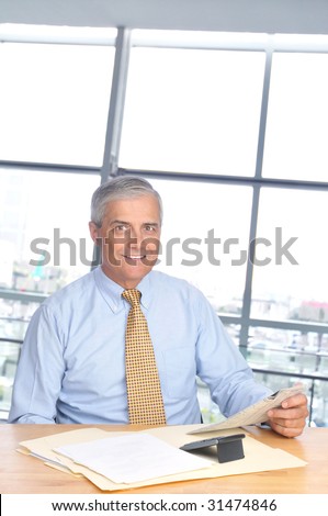 Smiling mature Businessman Seated at Desk with Newspaper and calculator in office setting