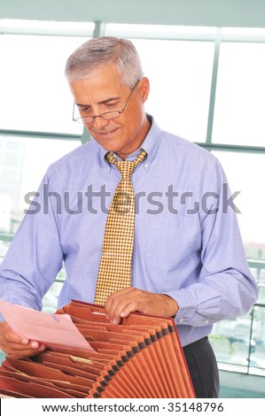 Mature Businessman Putting Papers in File Box in front of Office Window