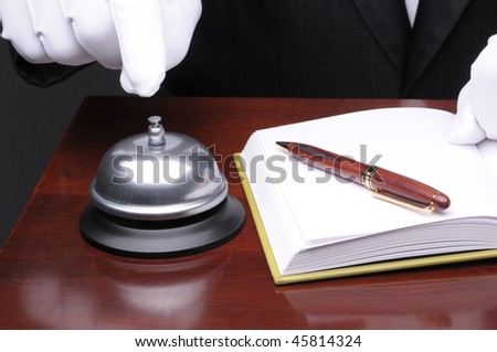 Close up of a Desk Clerk Ringing Service Bell at check in counter with pen and registration book
