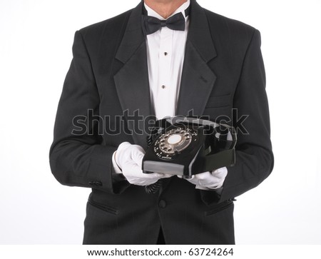 Butler in Tuxedo holding an old rotary telephone in front of his body. Torso shot only isolated over a white background.