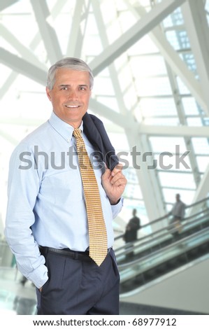 Middle aged businessman standing in front of an escalator with his jacket slung over his shoulder. Vertical format.