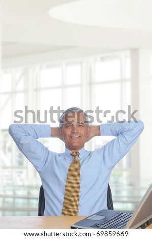 Businessman sitting at his desk in a modern office building with hands behind his head. Vertical Format