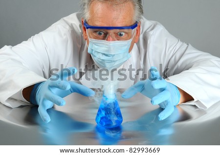 Closeup of a mad scientist as he observes a chemical reaction in his laboratory. Man is partially hidden behind a glass beaker that is bubbling over and smoking.