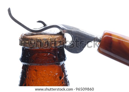 Macro shot of a brown beer bottle with an opener ready to pry up the bottle cap. Horizontal format over white.
