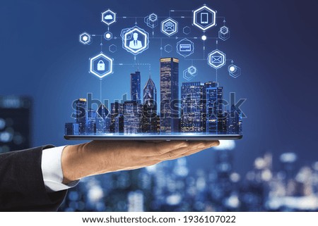 Internet of things in smart city concept with businessman hand holds digital tablet with night skyscrapers and digital social network icons
