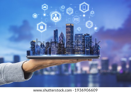 Cloud technology in smart city concept with human hand carries digital tablet with megapolis city skyscrapers and digital social network symbols above at blurry skyline background