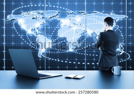 businessman standing in modern office and looking to global business map